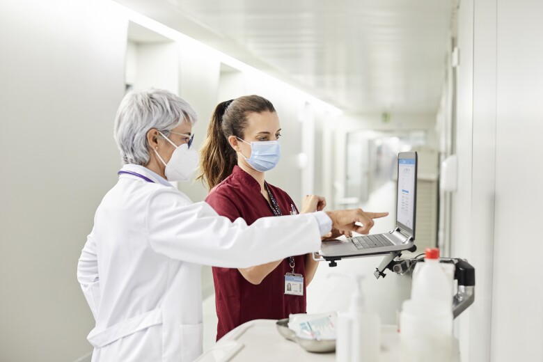 Healthcare professional in protective mask reviewing information on a laptop with a female nurse