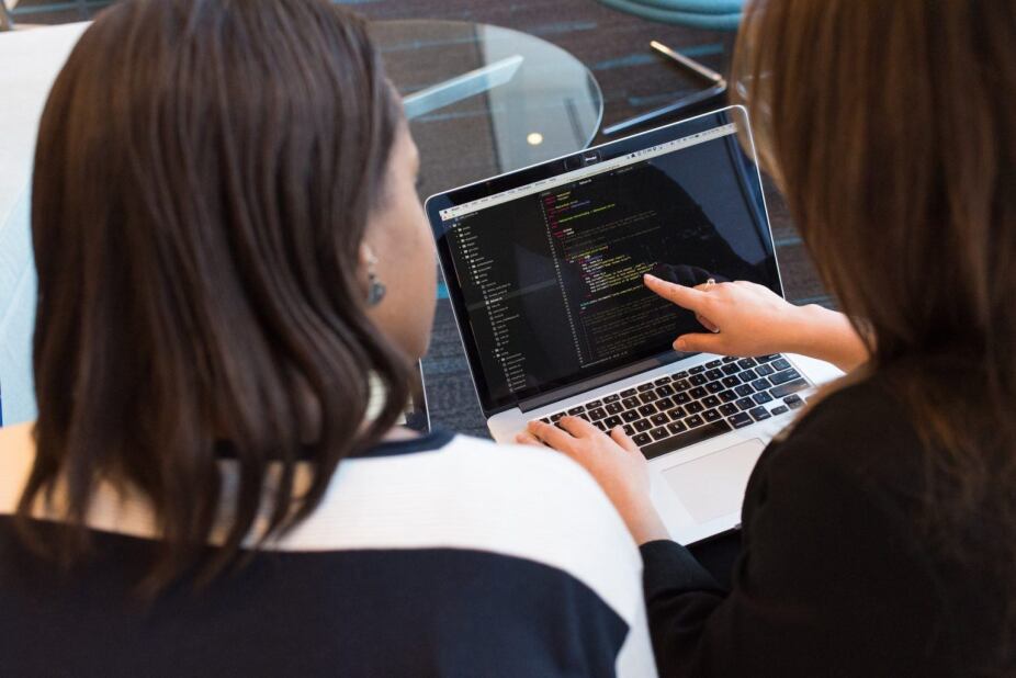looking over the shoulders of two software developers while they inspect code on a laptop