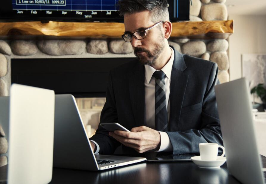 Serious business man accessing online learning resources from his mobile phone and laptop