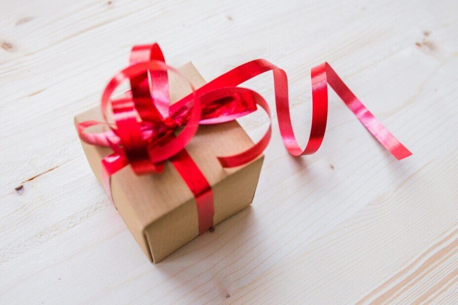 Small, simple gift on a wood floor, wrapped with basic brown cardboard and a red ribbon