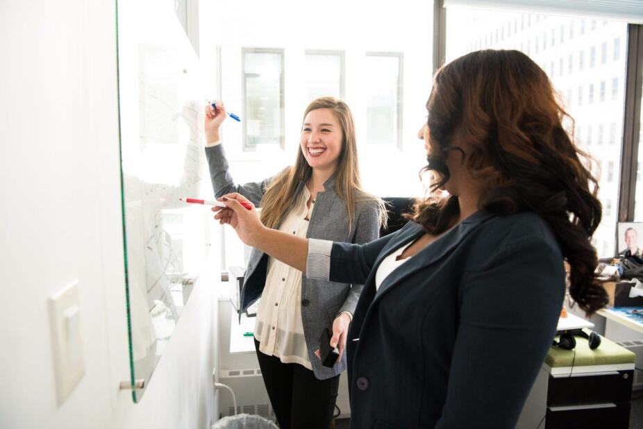 two female IT professionals white board their thoughts during a meeting