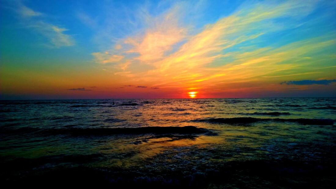 High-contrast sunset viewed from the shore as the ocean waves roll in