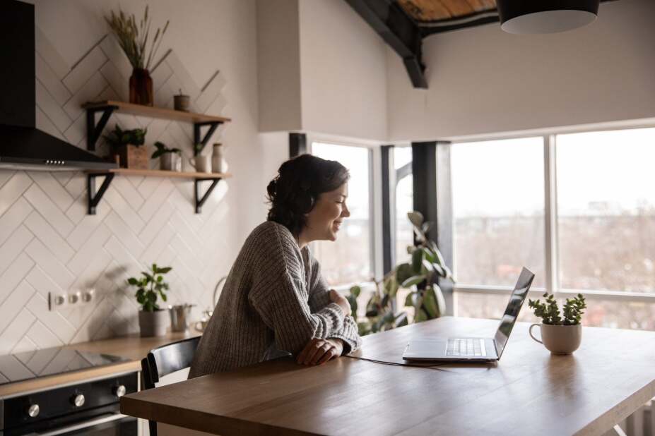woman laughing and chatting on a laptop in her home kitchen