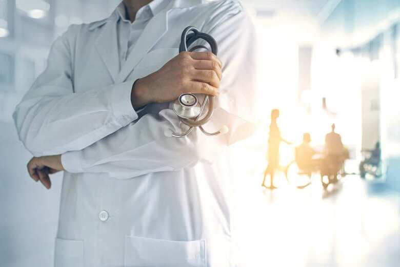 Doctor with arms crossed holding stethoscope in foreground of hospital hallway