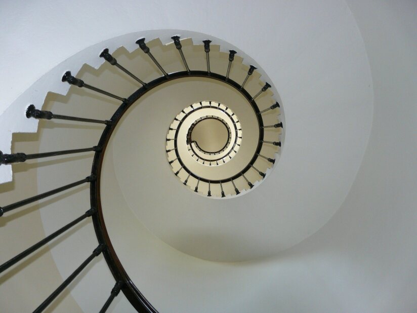 view looking up from under a white spiral staircase with a black railing