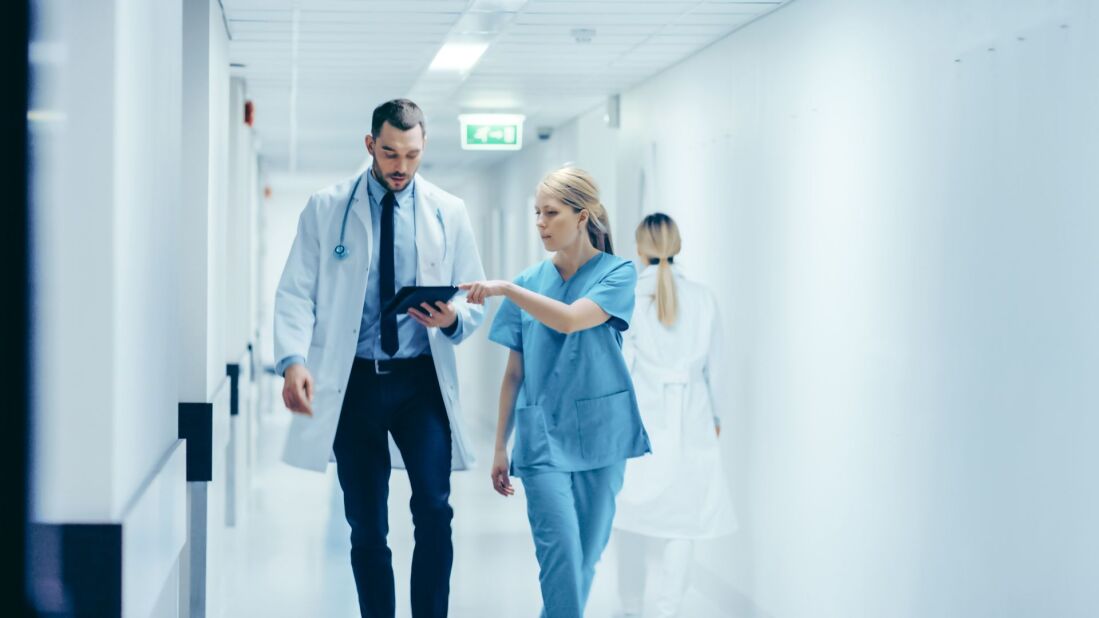nurse showing doctor information on a tablet while walking down hospital hallway