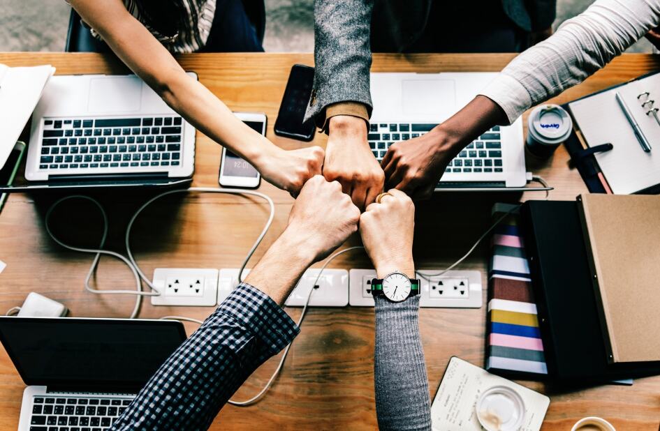 group of colleagues placing their fists together over the center of their workstation, showing teamwork