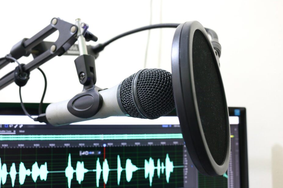 microphone used for podcasts and radio shows sits in front of a computer screen showing sound waves