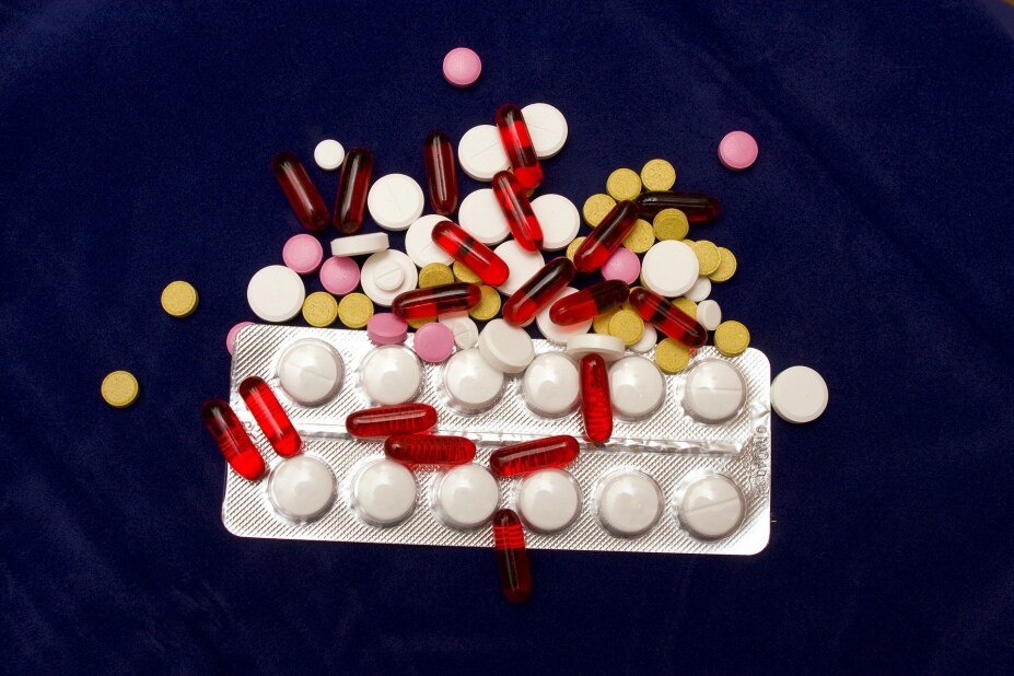 variety of prescription drugs in different shapes, sizes and colors scattered over a dark blue background