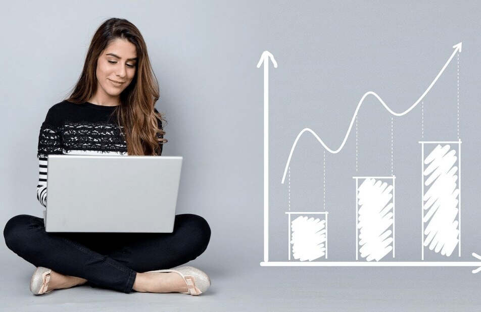 professional woman sitting on the floor with her laptop next to an illustration of a bar graph