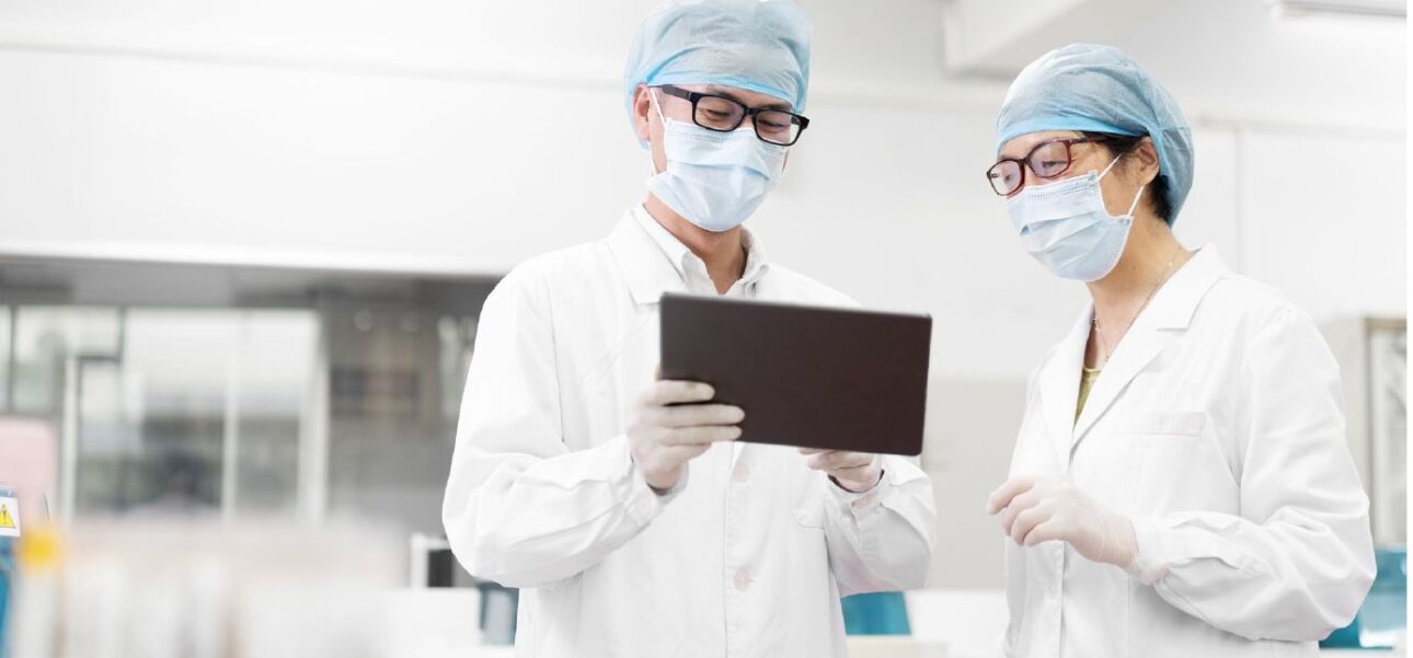 two doctors wearing personal protective equipment and reviewing patient information on a tablet