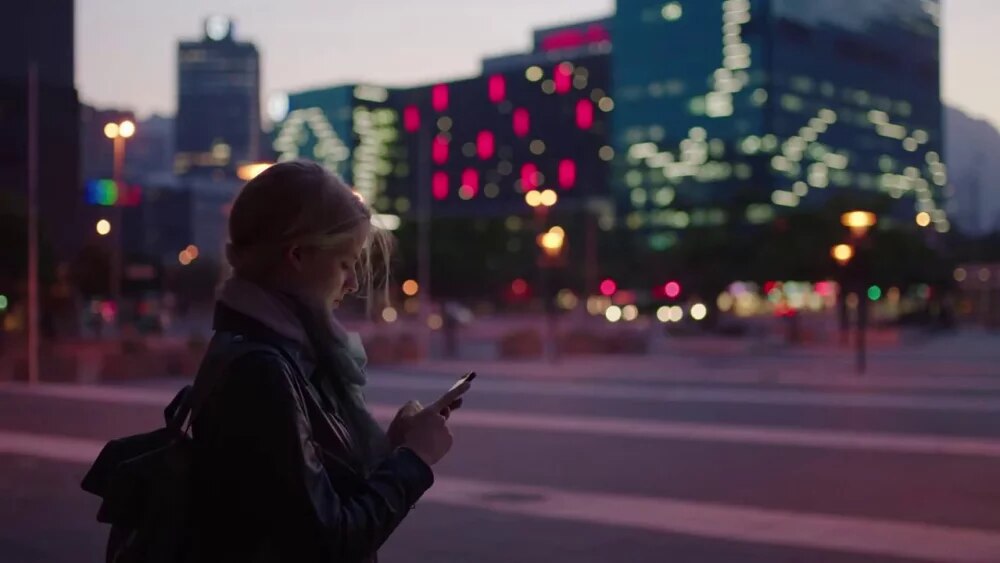 young woman outside in an urban setting at dusk looking at her phone