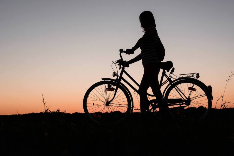 silhouette of a girl walking her bike across an open field at dusk