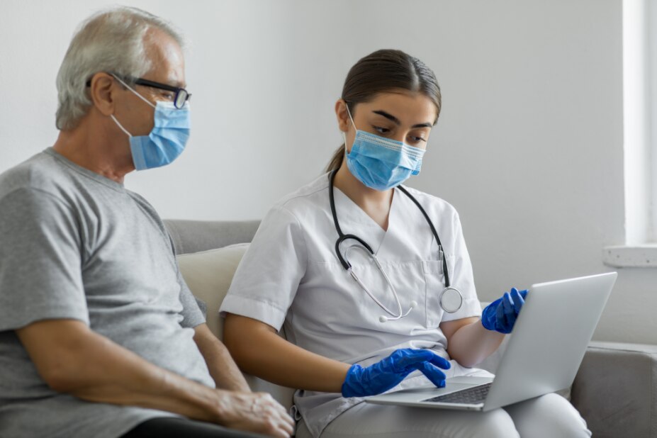 nurse reviews and confirms patient identity information on a laptop, both wear medical masks
