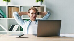 Young man smiling as he reads his laptop screen