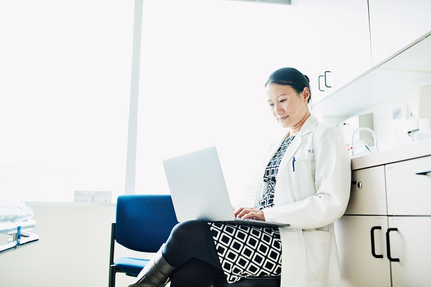 doctor entering patient information on her laptop in an exam room