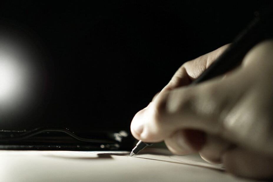 hand writing a note while a dim spotlight shines on the paper