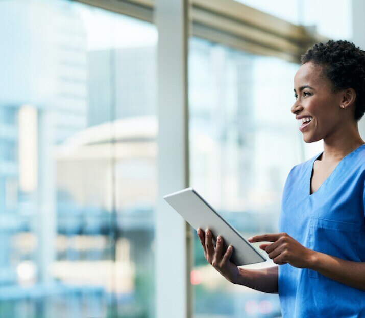 smiling nurse using tablet in hospital hallway