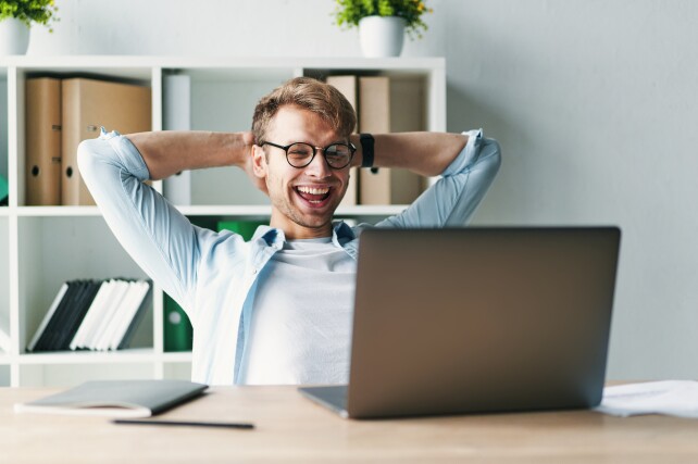 Young man smiling as he reads his laptop screen