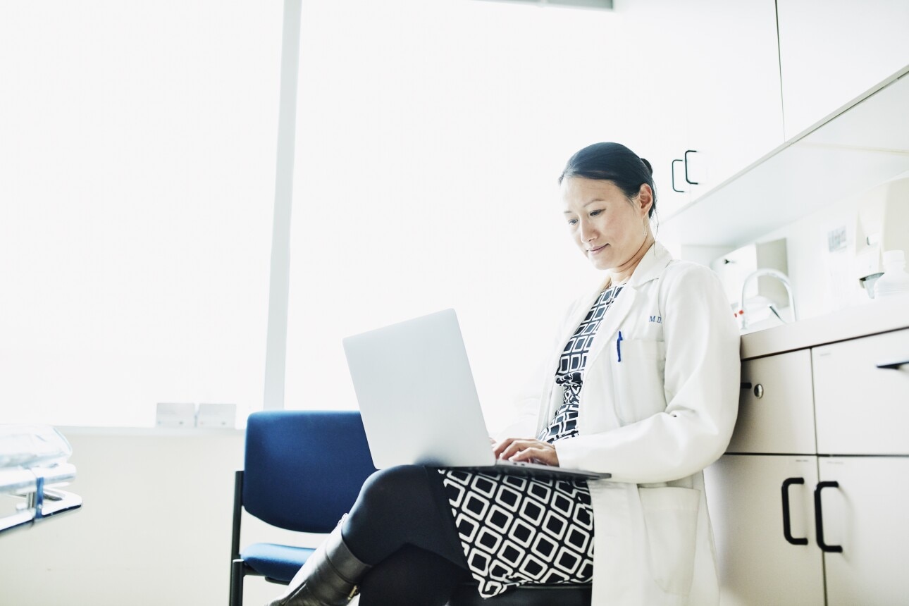 Portrait of female doctor working on laptop in exam room
