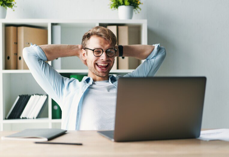Young man smiling as he reads his laptop screen