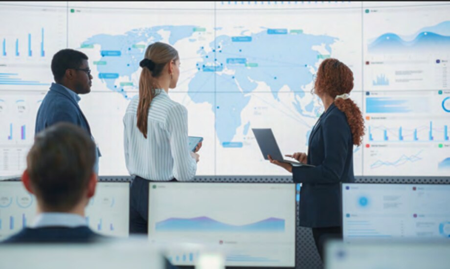 Three supply chain executives analyze supply chain data on a large map with several charts of data