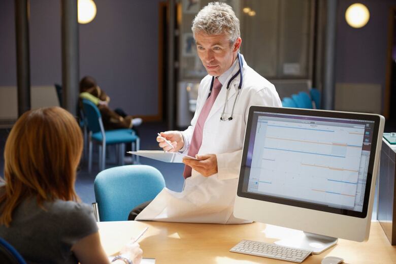 doctor sitting on desk talking to office receptionist