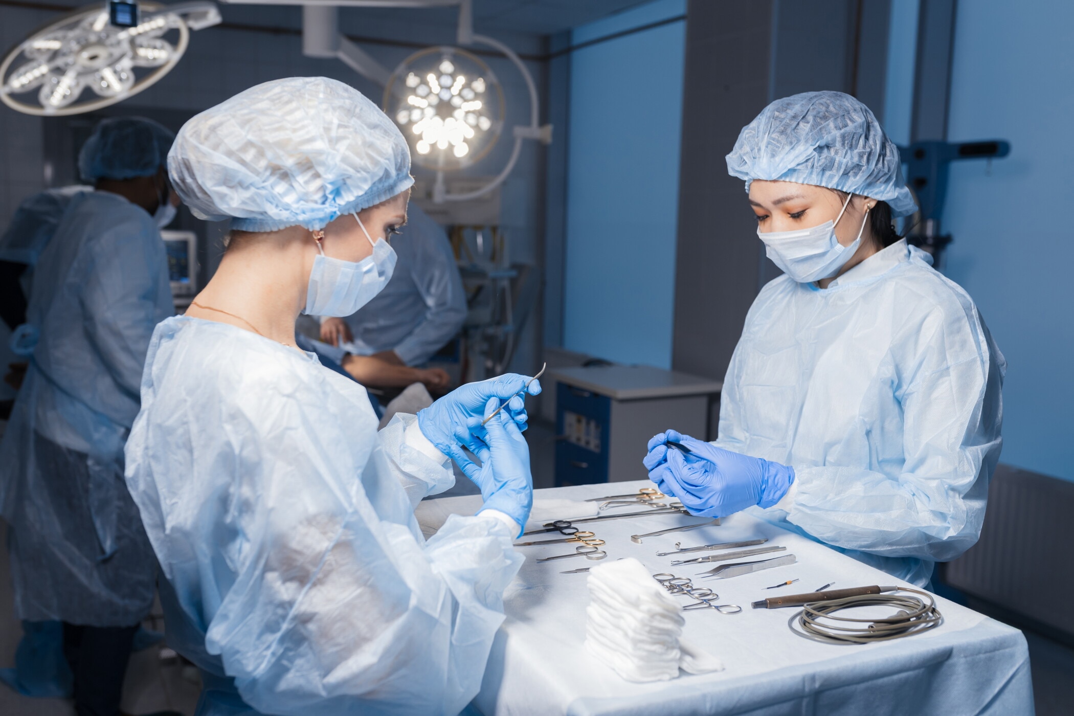 Two female assistants preparing surgical instruments and tools arranged on a table for a surgery, providing all necessary equipment to professional surgeons