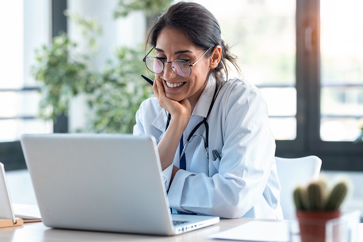 female doctor smiling while reading information on her laptop