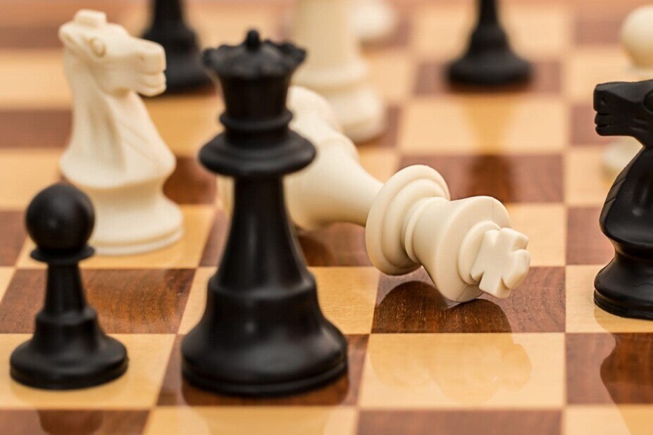 Wooden chess board with black and white chess pieces, the white king piece laid down