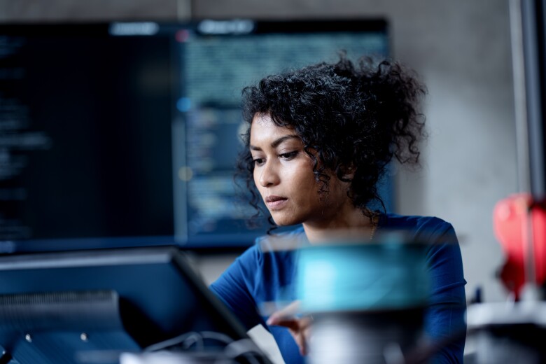 An Asian female software developer coding or debugging code on a computer at her desk in the tech office.