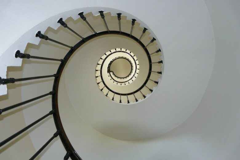 looking up through the center of a white spiral staircase with black railing