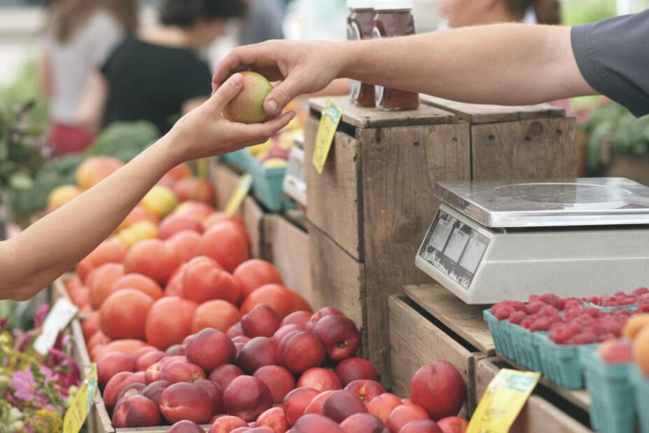 shopper at a farmer's market accepting an apple from a vendor
