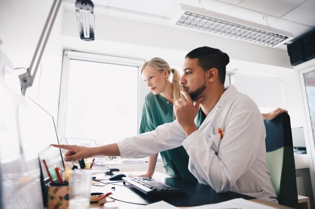 Young male doctor pointing at computer monitor to female nurse in office