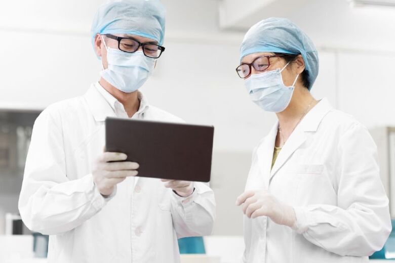 two doctors wearing personal protective equipment and reviewing patient information on a tablet