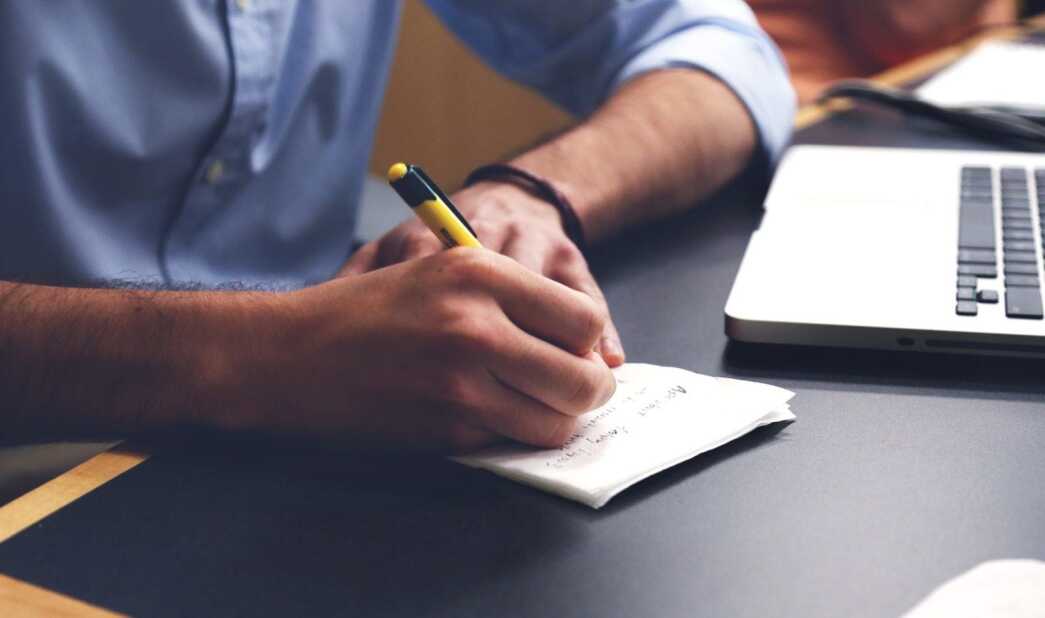 Close-up of a person's hands on their desk writing a note