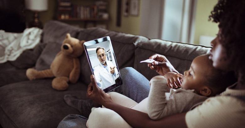 doctor on tablet talking to a caregiver holding a baby and a thermometer
