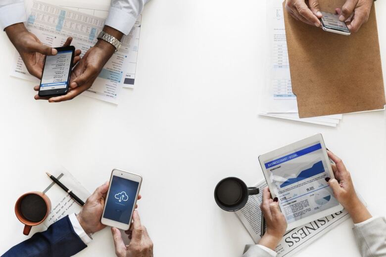 hands of four different people each holding a device and looking at business research