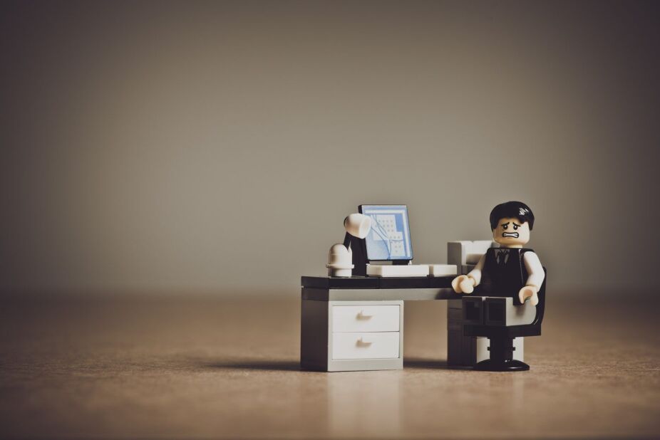 Portrait-style image of a Lego figure at a work desk with an anxious expression