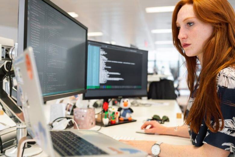 software developer working at her desk on multiple computer screens