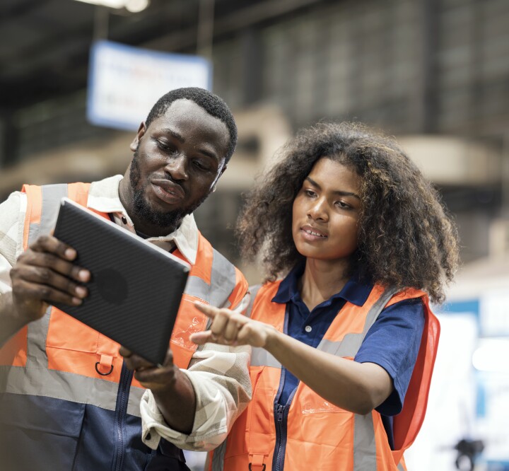 African American Production Control Engineers standing on the shop floor reviewing daily report on a tablet